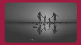 A family silhouette holding hands against a twilight sky, with their reflection shimmering on the tranquil water's surface.