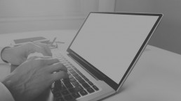 Black and white image of a person working on a laptop with a blank screen, suitable for adding customized content.