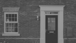 Monochrome portrayal of a classic brick facade featuring a stately black door and a window with white trim, encapsulating a timeless suburban elegance.